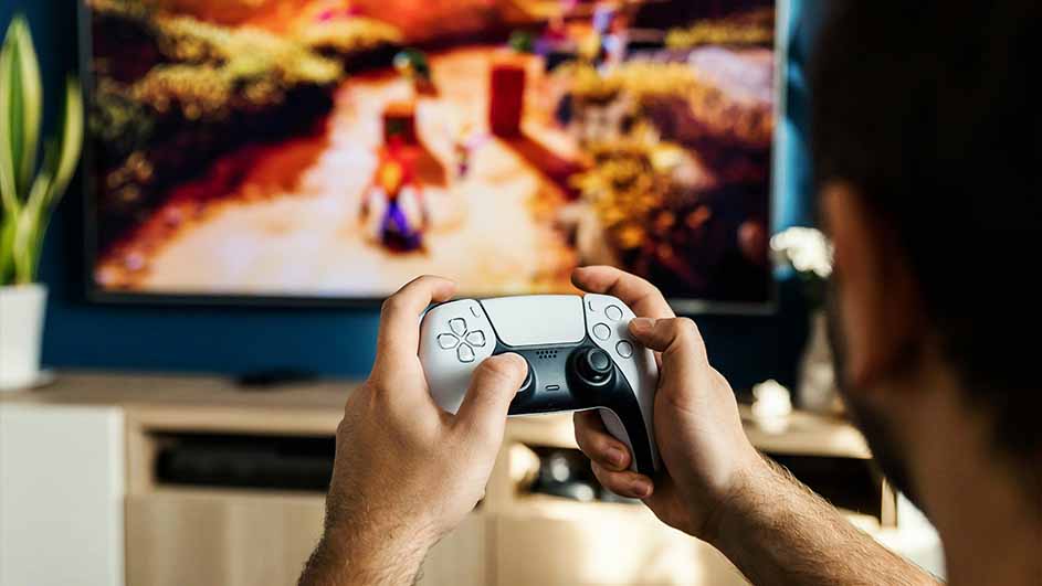 Een persoon speelt een videospel met een witte controller voor een tv. Op het scherm is een actiescène te zien.