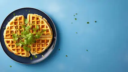 Een blauw bord met een wafel, verdeeld in vier stukken, gegarneerd met groene kruiden op een blauwe achtergrond.