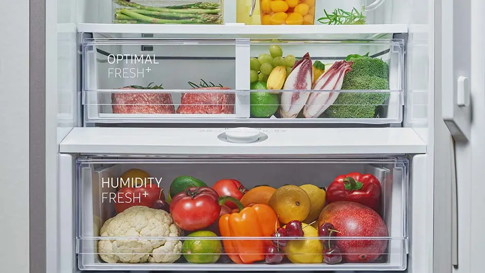 Koelkast met groenten en fruit in doorzichtige laden, zoals asperges, druiven, paprika's, tomaten en andere producten.