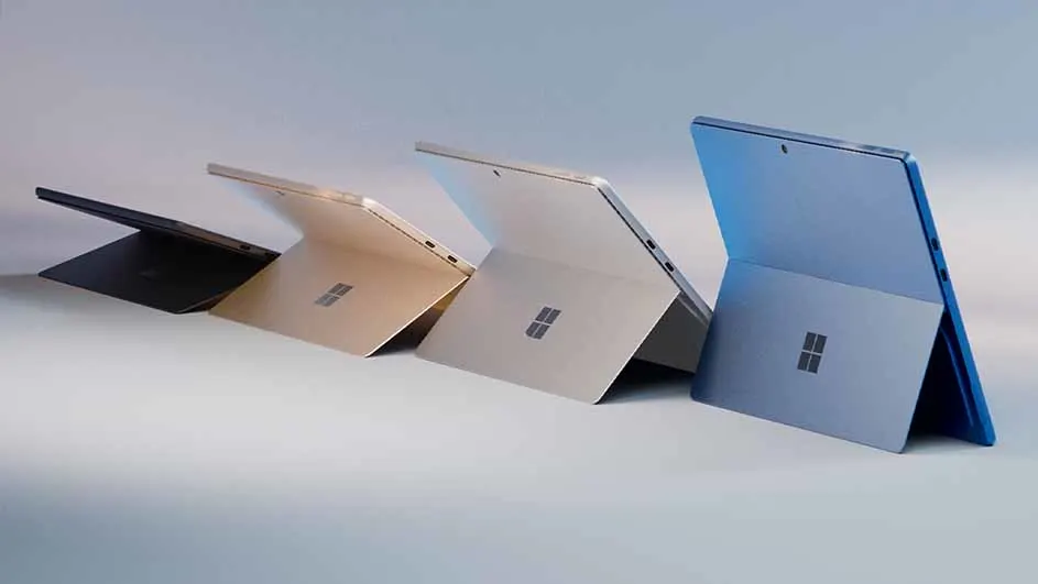 Rij van vier Microsoft Surface-tablets in zwart, goud, zilver en blauw, staand met uitgeklapte steunen op een witte ondergrond.