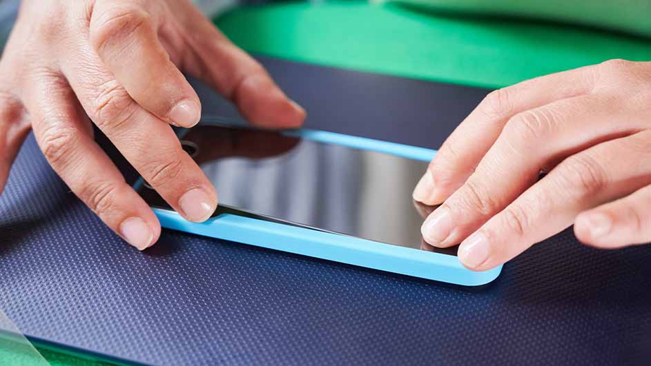 Twee handen plaatsen een blauwe telefoon op een blauwe ondergrond met een groene achtergrond.