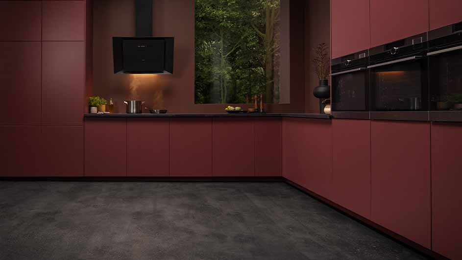 Een keuken met kastanjekleurige kasten, een zwarte afzuigkap en een zwart aanrecht. Er zijn twee zwarte ovens ingebouwd.