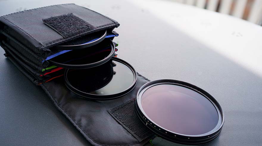 Zwarte camerlenzen liggen naast een open zwarte tas met gekleurde voeringen op een grijze ondergrond.