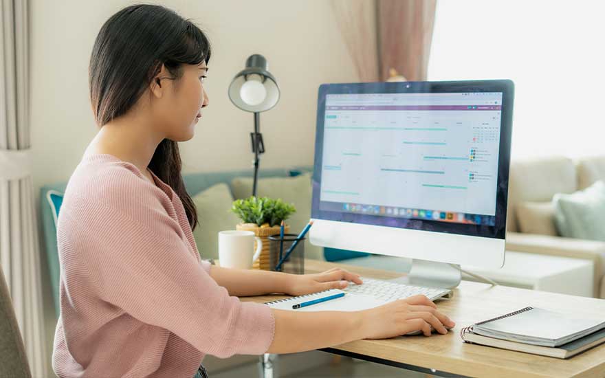 Vrouw werkt aan de computer thuis met notities en een kopje koffie naast zich.