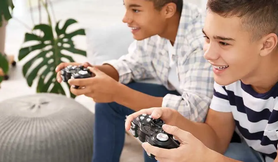 Twee jongeren zitten naast elkaar, geconcentreerd en lachend, terwijl ze samen gamen met controllers in hun handen.