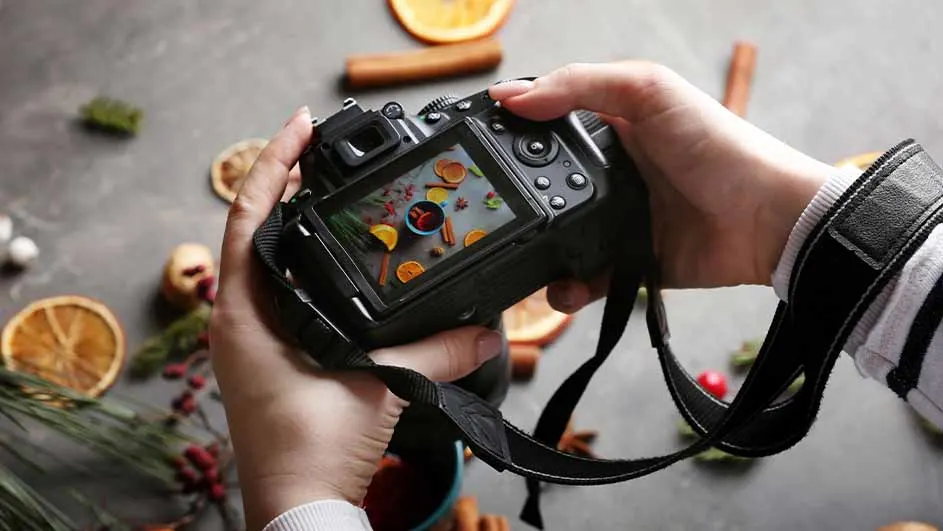 Een camera in handen met een foto van sinaasappelschijfjes, kaneelstokjes en rode bessen op het scherm.