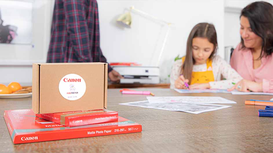 Doos en Canon-fotopapier op tafel. Een meisje en een volwassene tekenen. Printer en lamp op een witte achtergrond.