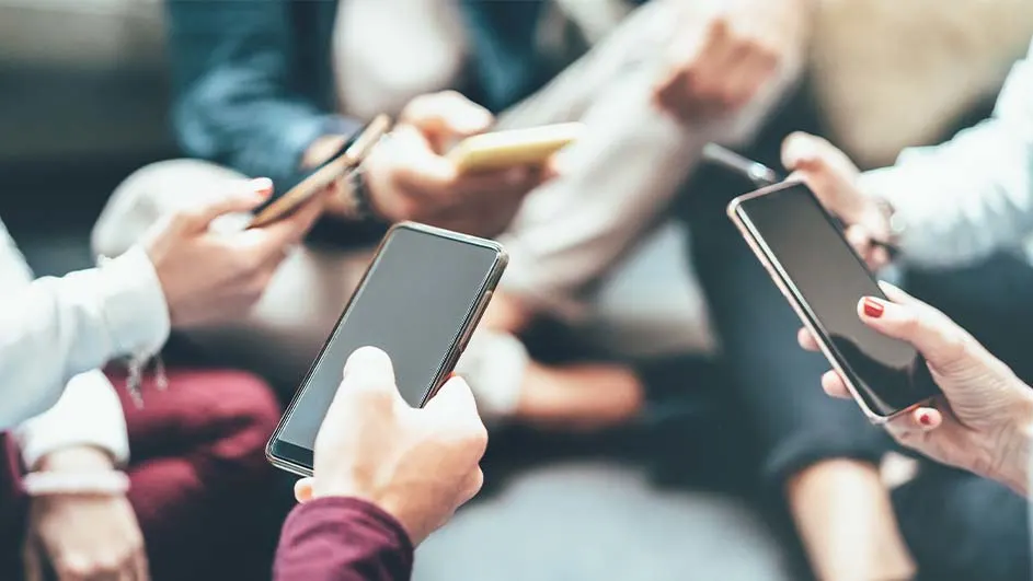 Groep mensen zit samen, elk met een smartphone in de hand. Kleding varieert, met jeans en truien zichtbaar.