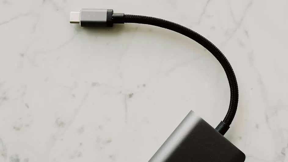 Een grijze USB-C-connector met een zwarte gevlochten kabel is aangesloten op een groter grijs apparaat op een witte achtergrond.