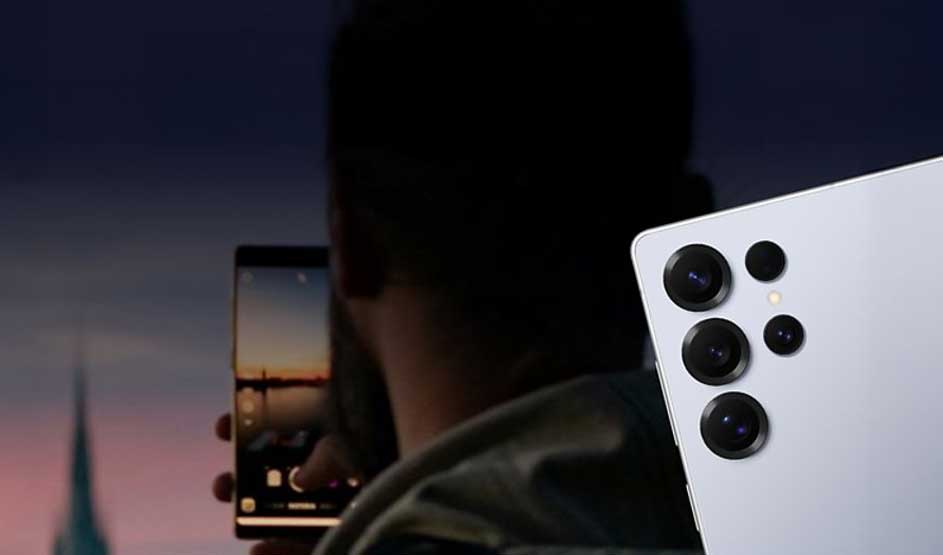 Een persoon maakt ’s avonds een foto met een witte Samsung smartphone met vijf camera’s, de stad is op het scherm zichtbaar.