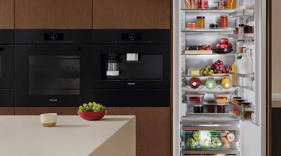 A modern kitchen featuring built-in Miele appliances and a well-stocked refrigerator. Storage jars containing pasta sit above the fridge. The wooden cabinetry provides a warm, inviting atmosphere.