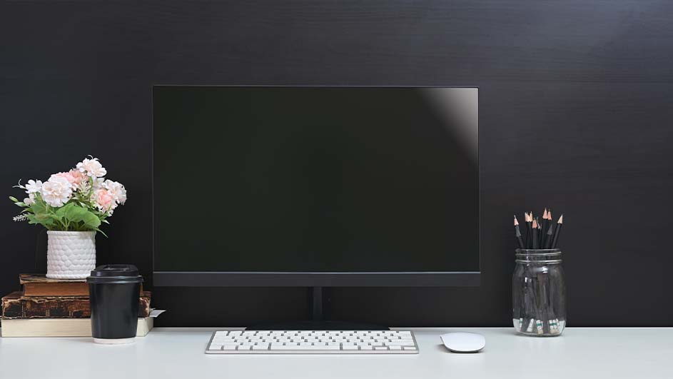 Een bureau met een computer, toetsenbord, muis, bloemen, boeken, beker en potlood in een pot. De achtergrond is zwart.