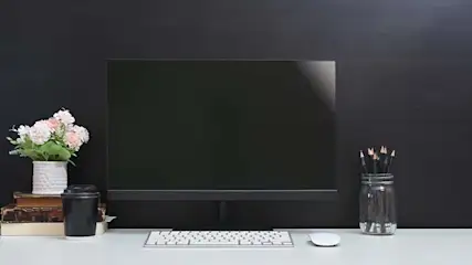 Een bureau met een computer, toetsenbord, muis, bloemen, boeken, beker en potlood in een pot. De achtergrond is zwart.