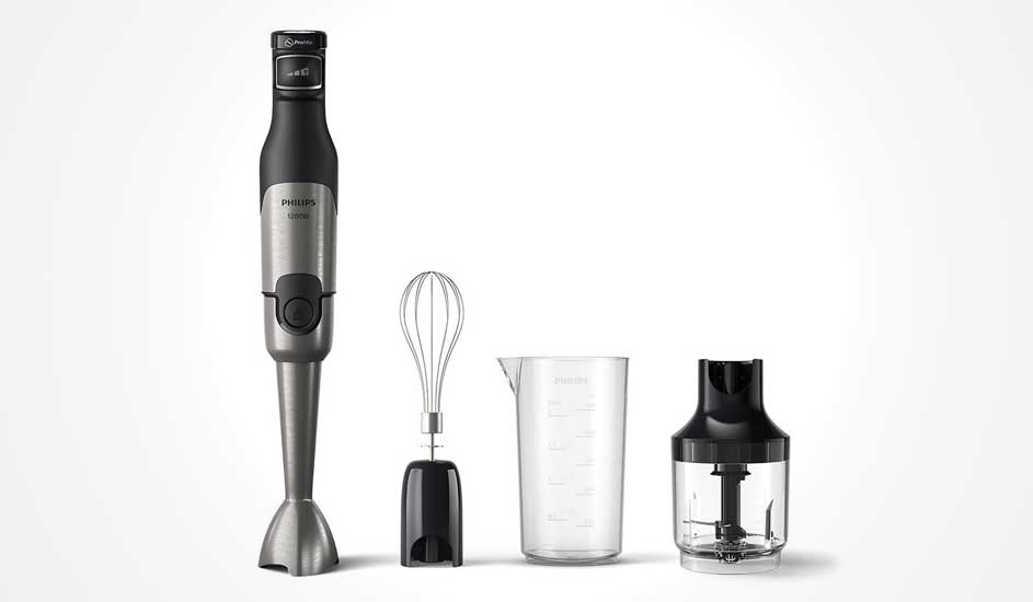 Donkergrijze Philips staafmixer met metalen voet, met ernaast een garde-opzetstuk, maatbeker en kleine hakmolen op witte achtergrond.