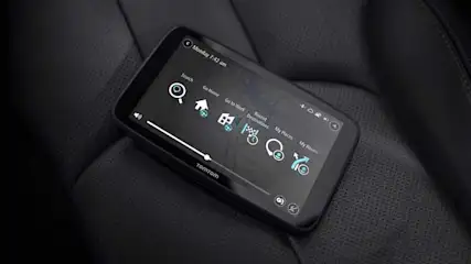 Een TomTom navigatiesysteem ligt op een zwarte, leren ondergrond met een scherm waarop menu-opties staan.