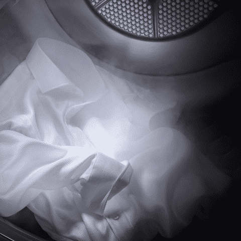 Wit overhemd in een wasdroger, met een metalen filter zichtbaar aan de bovenkant.