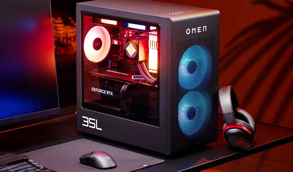 Compact gaming PC with glass side, RGB-lit components and GeForce RTX card, plus mouse, monitor and headset on dark desk.