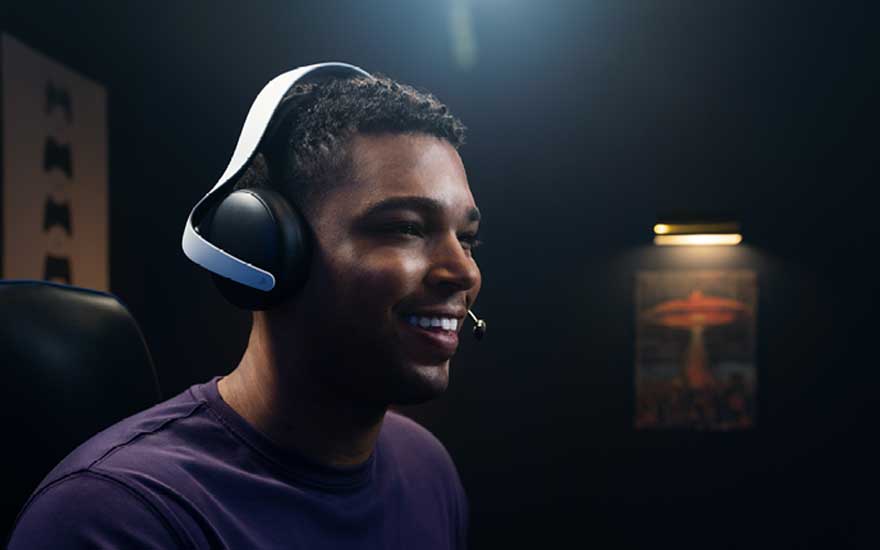 Een glimlachende speler draagt een grote gaming headset met microfoon in een donker verlichte kamer, klaar om online met teamgenoten te praten.