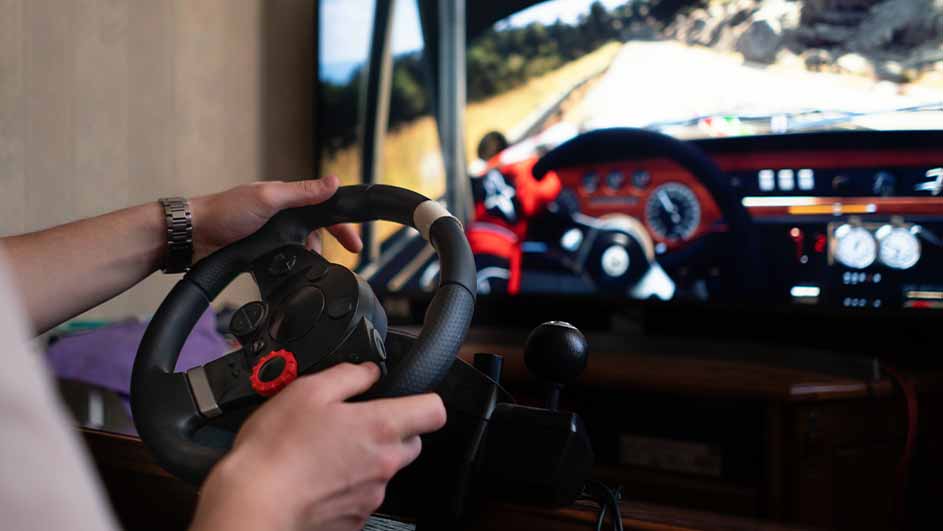 Een persoon gebruikt een zwart stuurwiel voor een racesimulatie, met een tv-scherm dat de race weergeeft.
