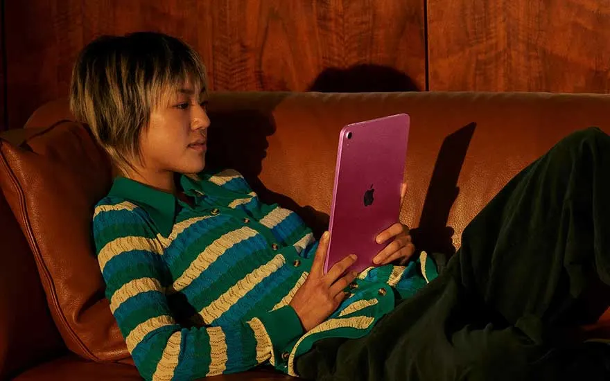Person lying on a leather sofa, holding a purple tablet upright, fully absorbed in whatever they are watching or reading.