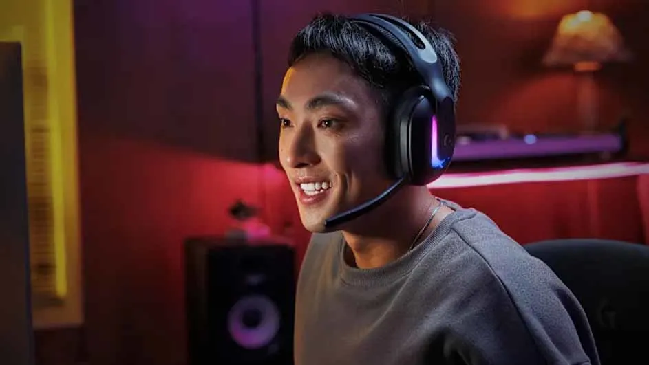Man die glimlacht tijdens het gamen, met een Logitech G gamingheadset met RGB-verlichting in een warm verlichte kamer.
