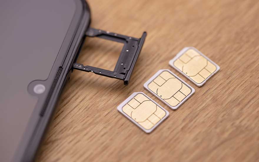 Drie SIM-kaarten liggen naast geopende SIM-lade van smartphone op houten oppervlak, toont dual-SIM functionaliteit.