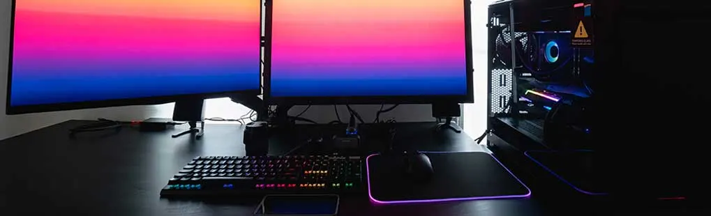Strakke gamingopstelling met drie schermen, RGB-toetsenbord, muismat en verlichte pc-kast op een donker bureau.