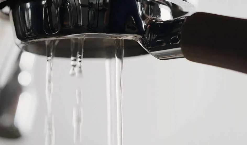 Op de afbeelding stroomt water uit een metalen filterdrager van een espressomachine. Het merk is op deze afbeelding niet zichtbaar.