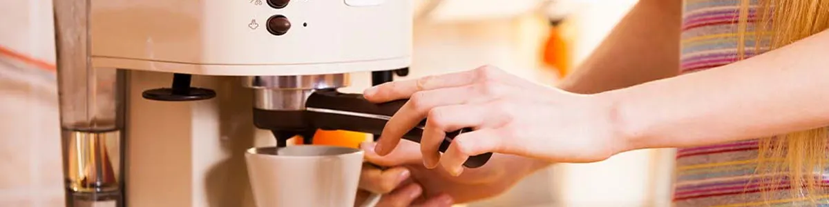A hand operates an espresso machine with a white cup underneath, ready to brew coffee in a warm kitchen environment.