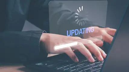 Iemand typt op een laptop met een voortgangsbalk en de tekst 'Updating' op het scherm.