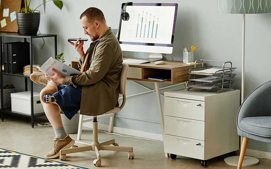 Man leest een document en spreekt in zijn telefoon bij zijn bureau met computer.