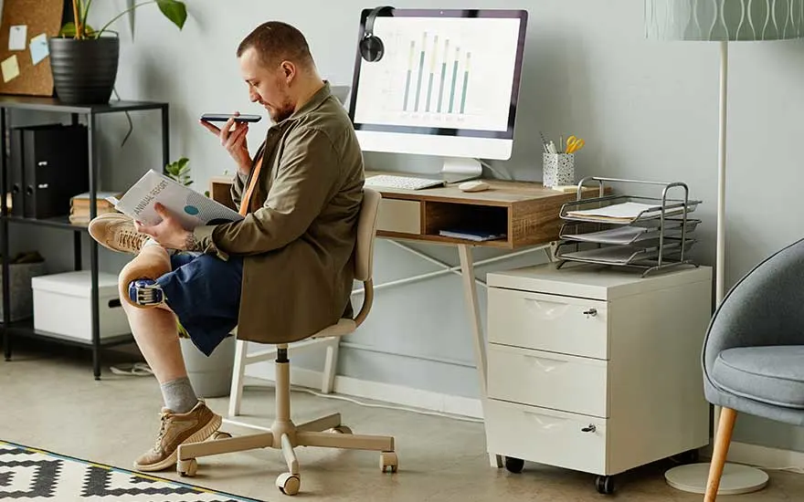 Man leest een document en spreekt in zijn telefoon bij zijn bureau met computer.