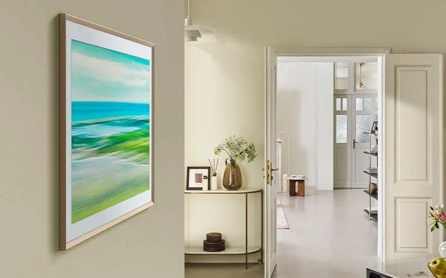 Een televisie met een schilderij van zee en lucht hangt in een lichte kamer bij een deur en een elegante hal met bloemen.