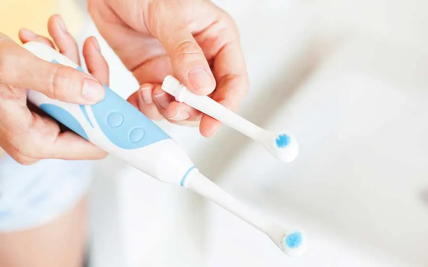 Hands replace the brush head of a white and blue electric toothbrush in a bright, clean and minimalist setting.