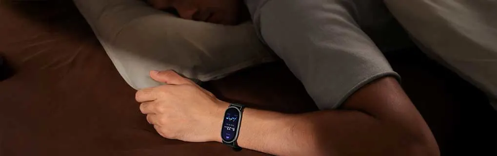 Een slapende persoon ligt op een donker bed, met een slimme fitnesshorloge om de pols die 's nachts zijn slaap registreert.