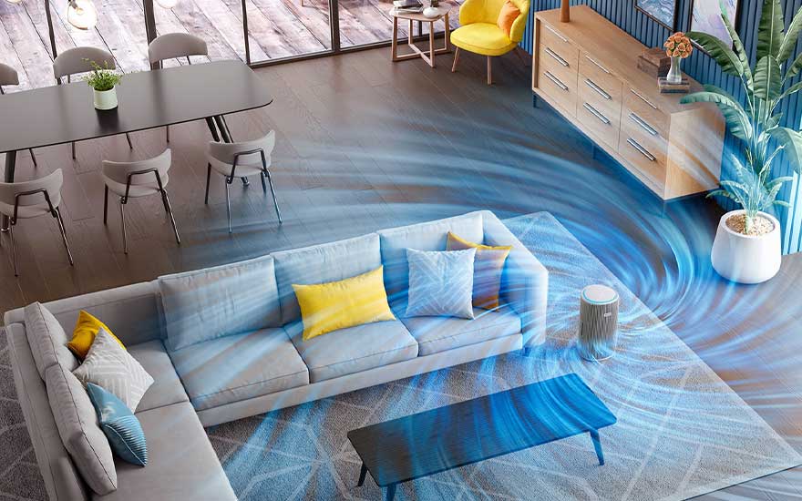 Moderne woonkamer met hoekbank en kleurrijke kussens, waar een compacte luchtreiniger blauwe luchtstromen rond de sofa en tafel laat cirkelen.