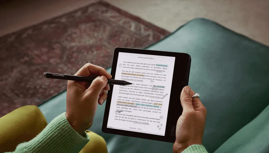 Handen houden een e-reader met tekst en markeringen vast, met een stylus in de linkerhand, op een groene stoel.