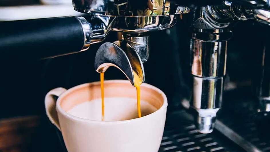 Espresso stroomt uit een zilverkleurige machine in een witte mok, op een donkere achtergrond.