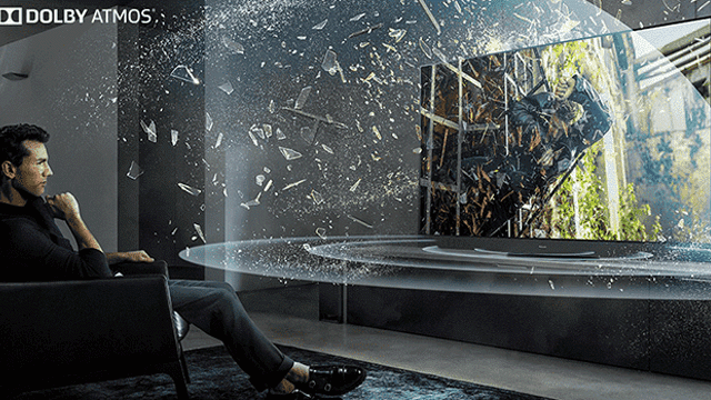 Een man zit in een stoel voor een tv met een gebarsten scherm en Dolby Atmos logo.
