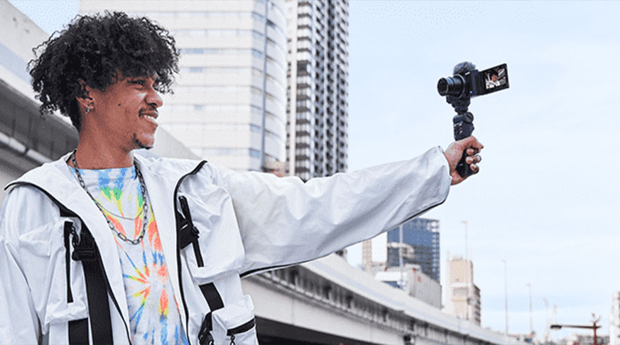 Een persoon filmt met een camera in een stedelijke omgeving met hoge gebouwen op de achtergrond.