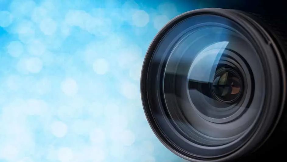 Een close-up van een cameralens met een blauwe, vage achtergrond. De lens is zwart en zilverkleurig.