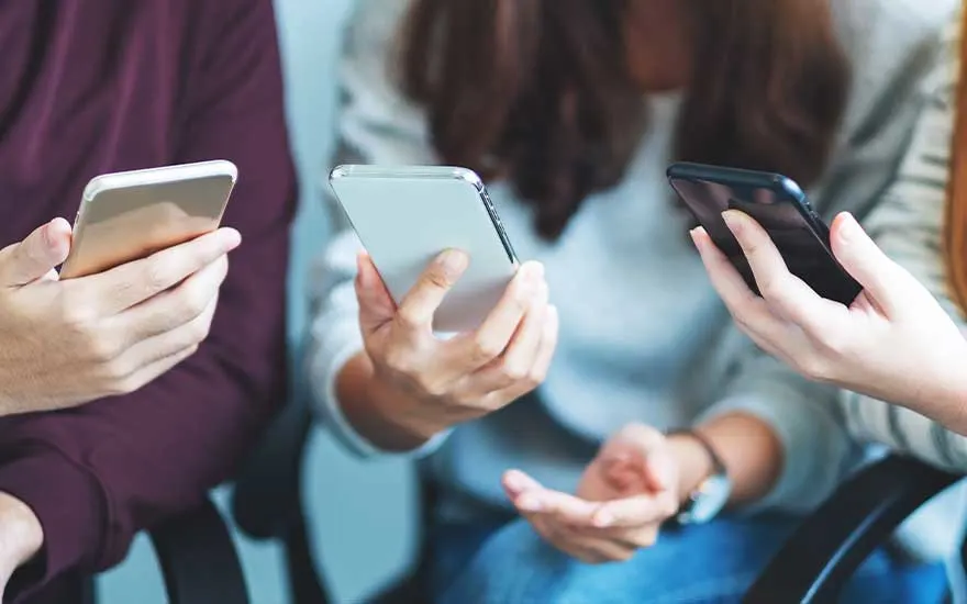 Drie paar handen houden verschillende smartphones vast, close-up shot met onscherpe achtergrond van mensen.