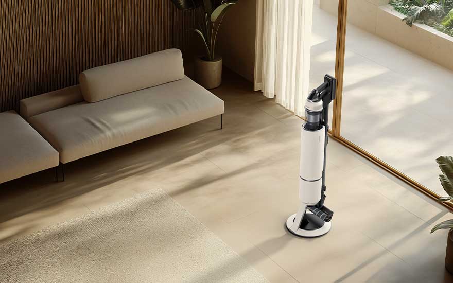 Een witte steelstofzuiger op slanke standaard staat in een zonnige woonkamer met beige bank, grote ramen en warme, minimalistische inrichting.