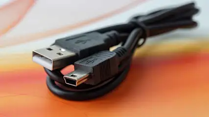 Een zwarte USB-kabel met een standaard en een mini-USB-connector ligt op een oranje ondergrond.