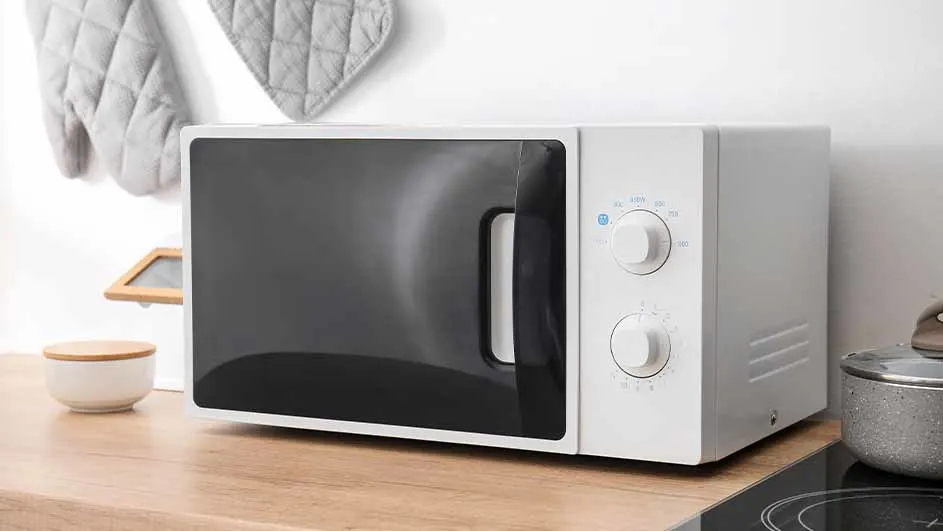 Een witte magnetron met een zwarte deur staat op een houten aanrecht naast een pan en keukengerei.