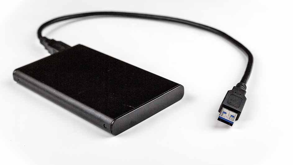 Een zwarte externe harde schijf ligt op een witte achtergrond met een USB-kabel eraan vast.