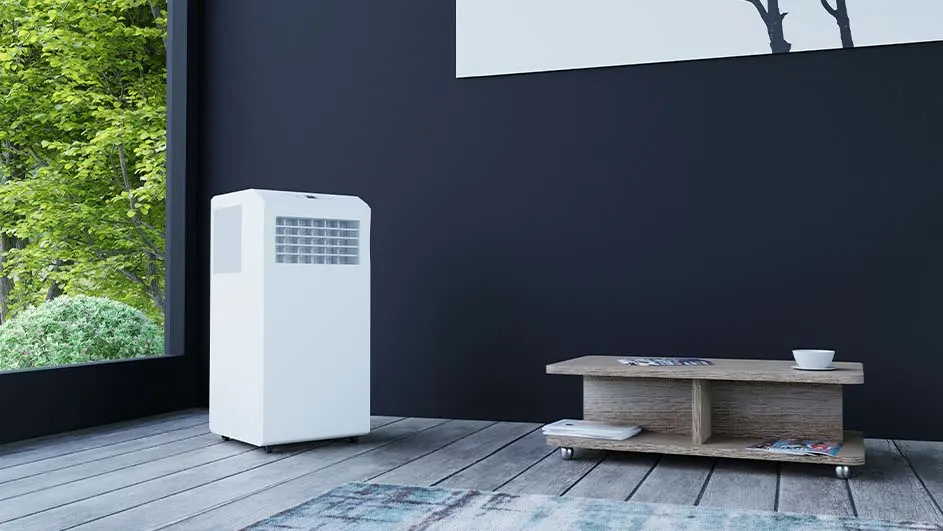Een witte airconditioner staat naast een raam met groen uitzicht, naast een lage houten tafel.