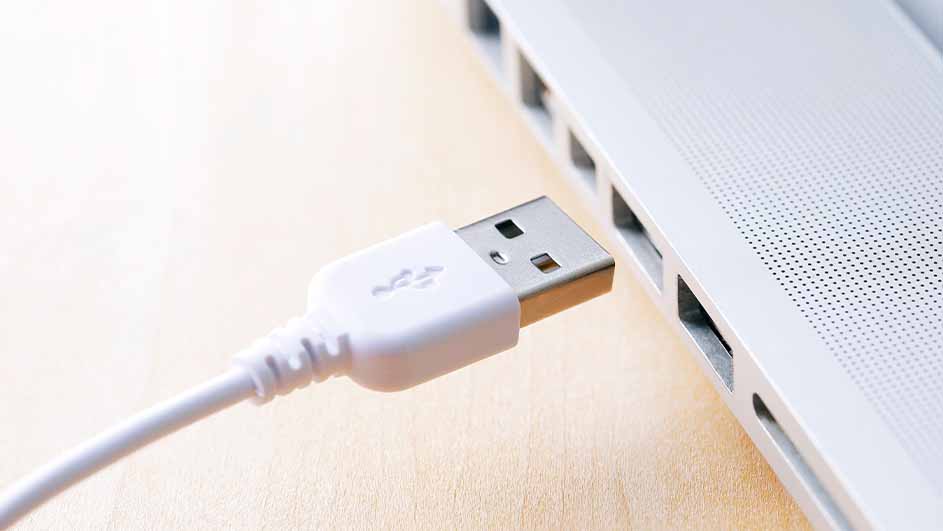 Witte USB-stekker gedeeltelijk in een zilverkleurige laptop gestoken op een houten tafel.