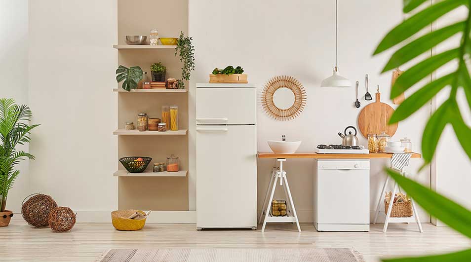 Een lichte keuken met witte koelkast, open planken, kamerplanten, rieten manden, een wasbak en houten details in rustige stijl.