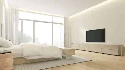 Slaapkamer met groot raam, wit beddengoed, houten vloer, televisie aan de muur en dressoir.